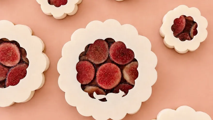 Pâtisseries festonnées garnies de figues, vues du dessus sur un fond rose.